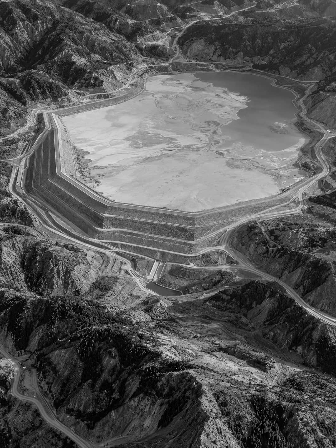 Aerial view of a tailings storage facility with a terraced embankment dam and a settled pond.